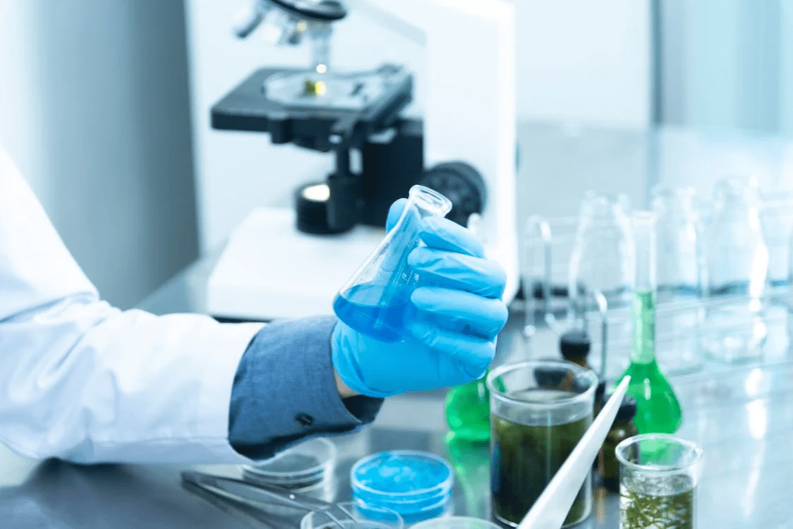 Scientist inside a laboratory holding a beaker filled with blue coloured liquid